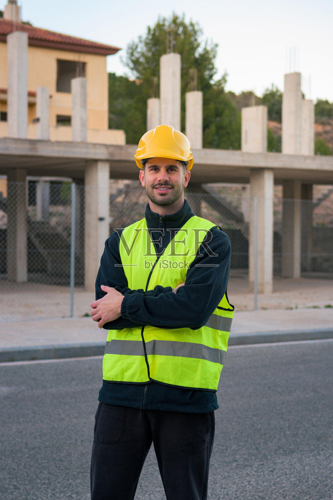 身穿反光背心、头戴黄色头盔的工人微笑着看着背景是施工现场的镜头照片摄影图片