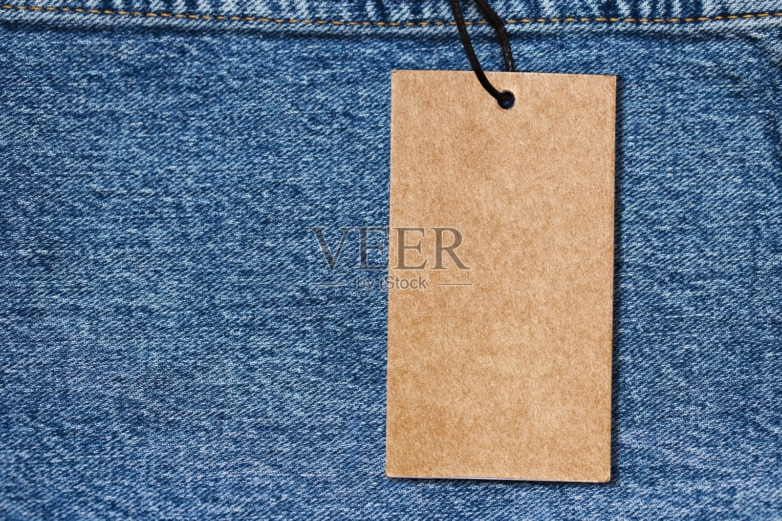 带有空白复制空间的时尚背景。空白棕色环保纸标签标签。蓝色牛仔裤牛仔纹理与线缝线。棕色衣服标签。照片摄影图片