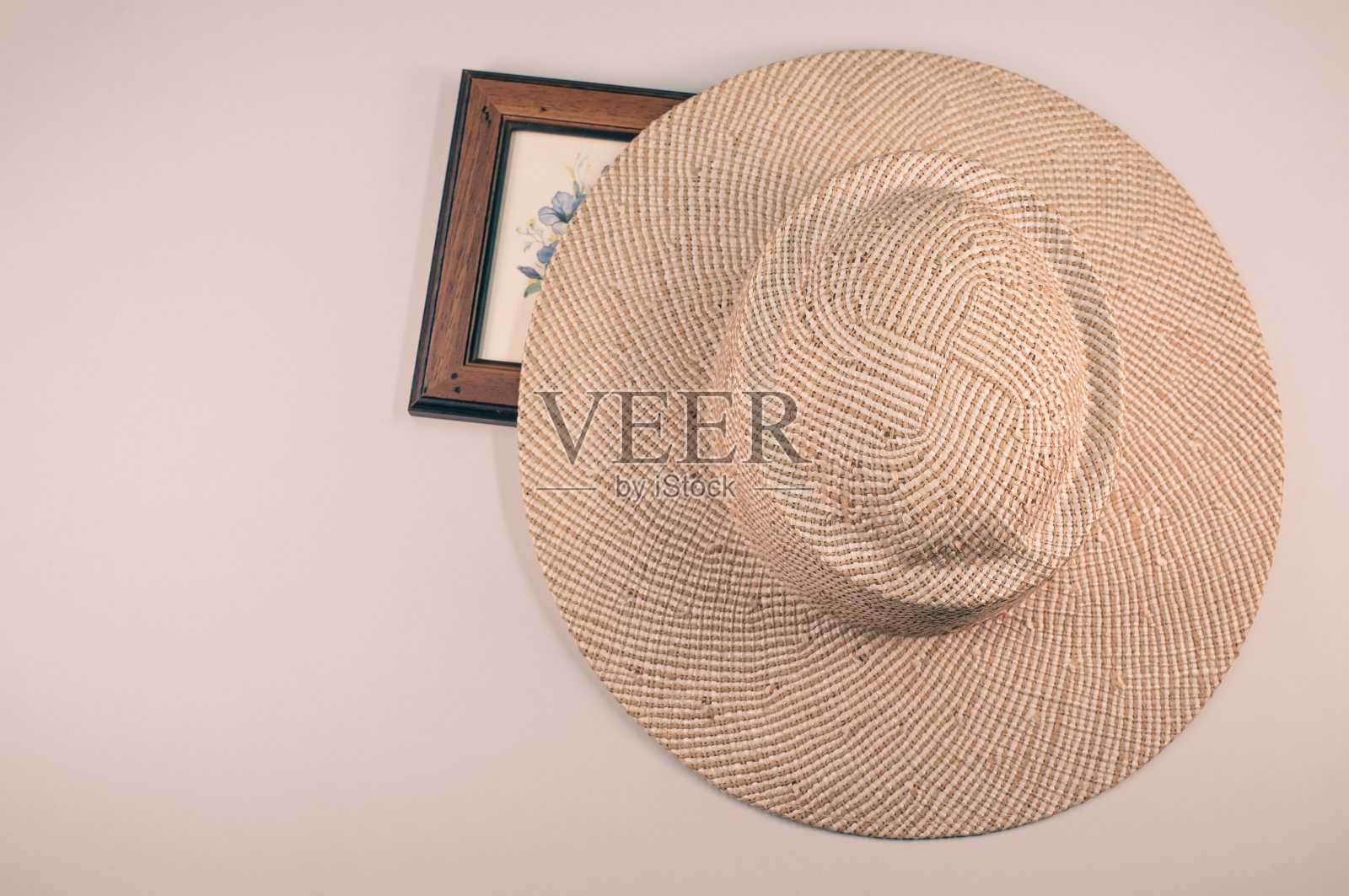 近距离的草帽和蓝色的花画与木框，在一个粉红色的表面照片摄影图片