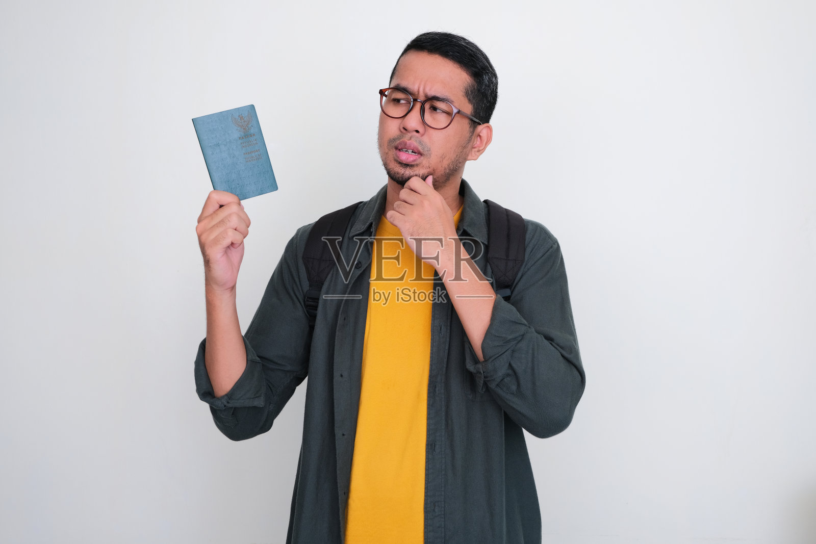 成年亚洲男子背着双肩包，带着困惑的表情看着他持有的印度尼西亚护照照片摄影图片