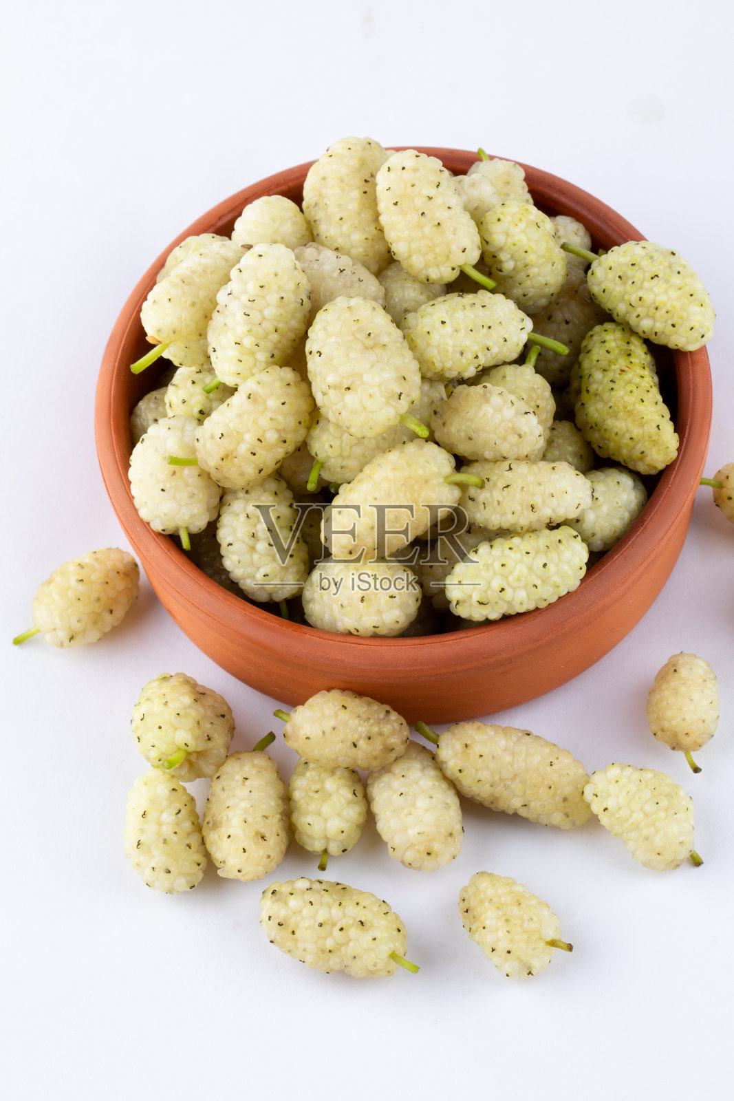 在明亮的白色背景上，一堆新鲜的白色桑葚放在陶罐里照片摄影图片