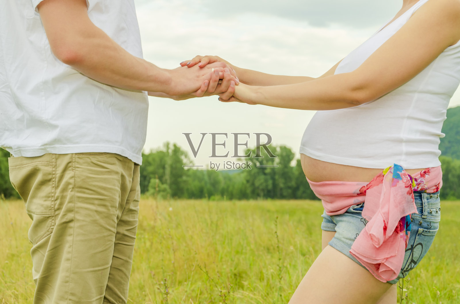 一对年轻男女，孕妇牵着手，在远处照片摄影图片