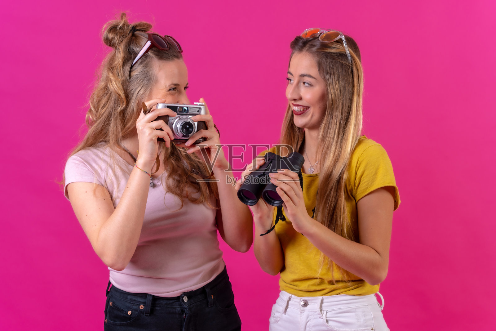 两个年轻的金发白人女性在夏天微笑着看度假照片，孤立在粉红色的背景上照片摄影图片