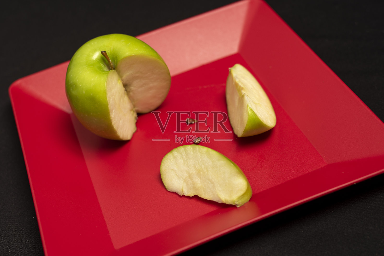 桌子上的红盘子上一个切好的绿苹果的特写照片摄影图片