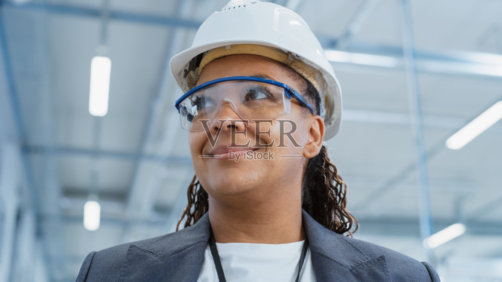 一个中年，快乐的黑人女工程师戴着白色安全帽，站在电子制造工厂。重工业专家在镜头前摆姿势。照片摄影图片