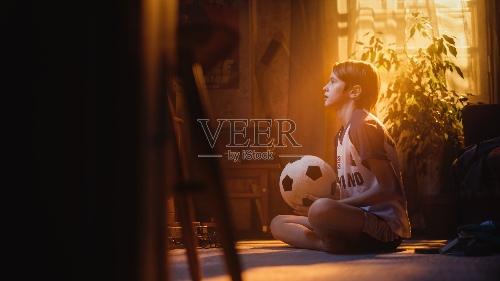 一个年轻的足球迷在家里看电视比赛的肖像。英俊的男孩支持他最喜欢的足球队，当球员进球时感到自豪。快乐童年概念。照片摄影图片