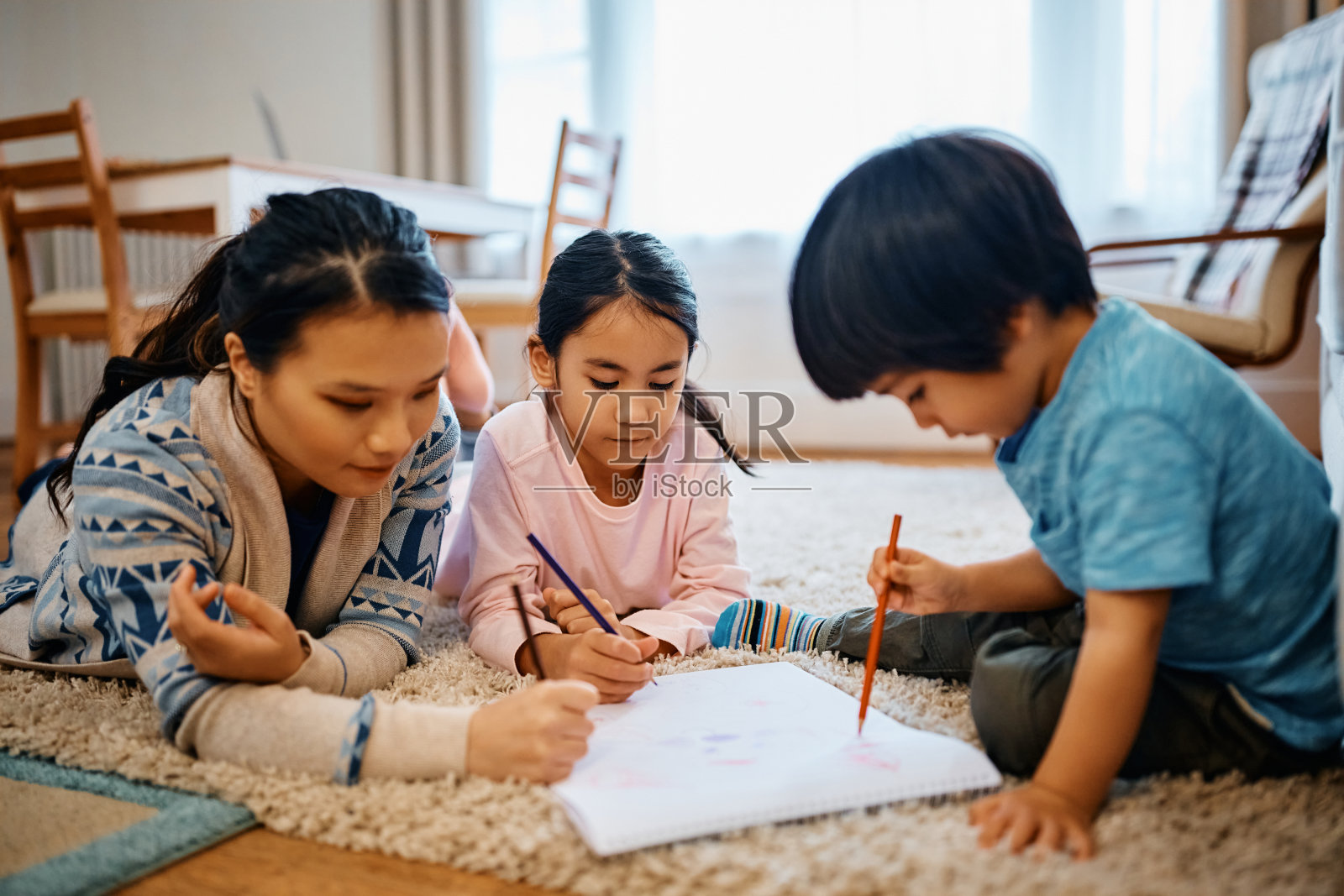 亚洲单身母亲在家里的地毯上休息时和她的孩子们一起涂色。照片摄影图片