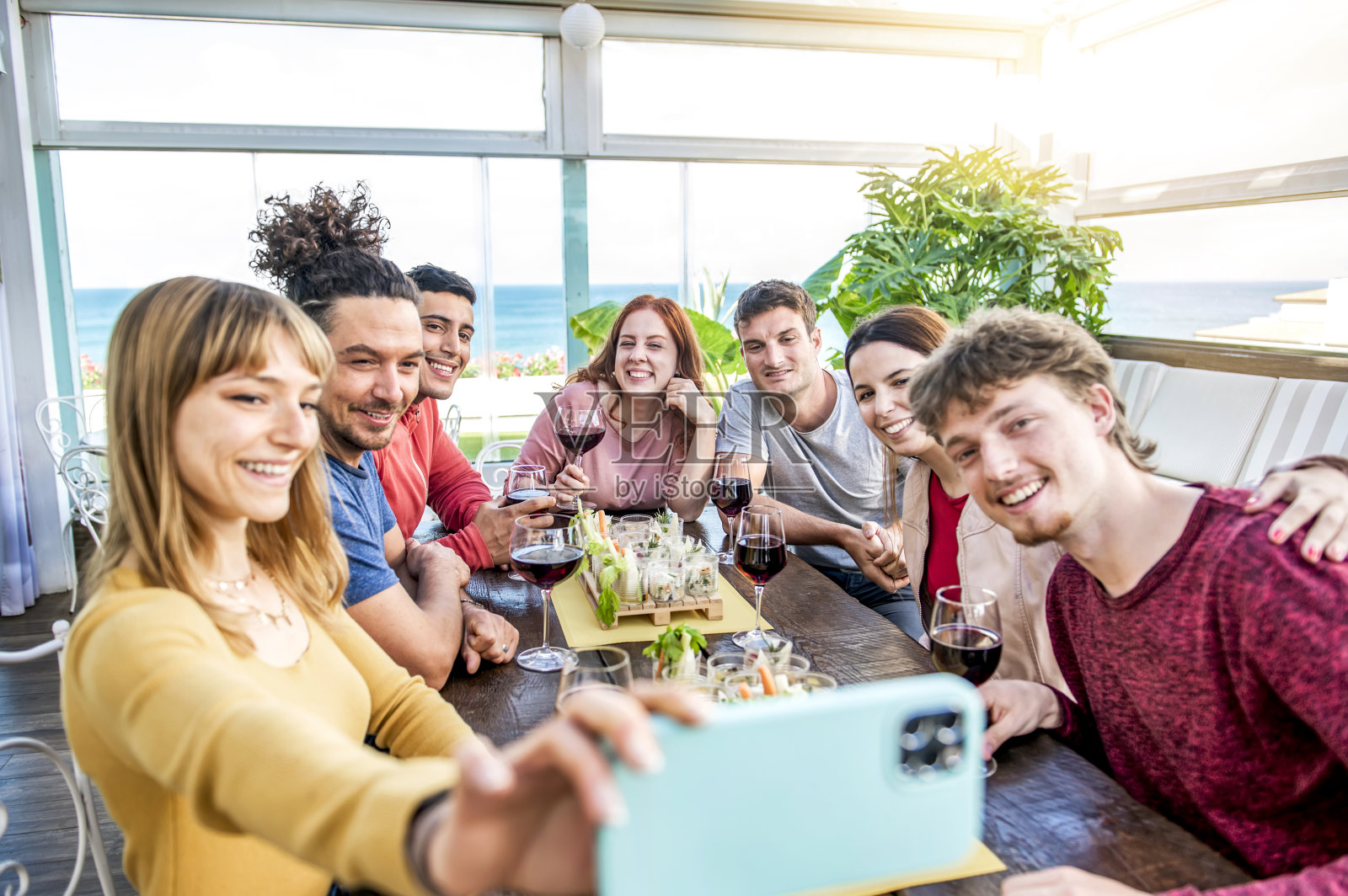 快乐的朋友们在露台上用智能手机拍照-年轻人敬酒和欢呼开胃酒喝红酒-用餐，乐趣和青年友谊的概念照片摄影图片