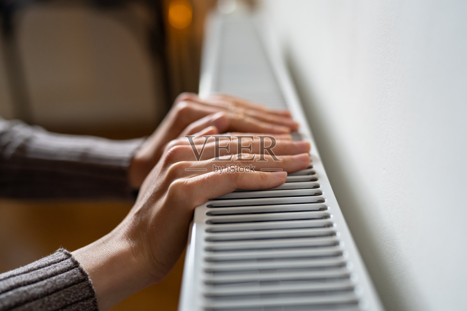 在寒冷的公寓里，穿毛衣的女人把手放在房间的中央供暖电池上取暖照片摄影图片