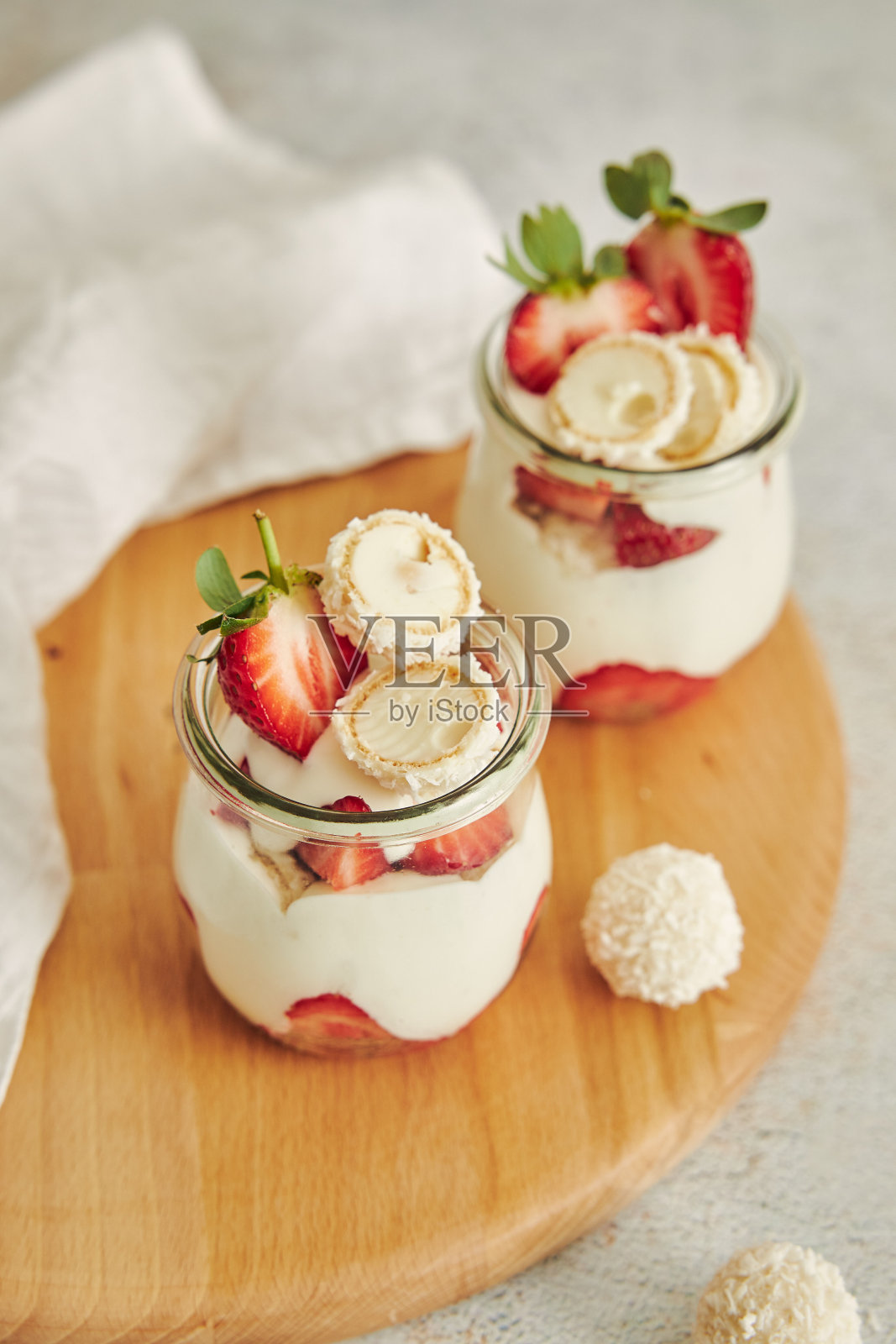 美味的奶油甜点，椰子松露和草莓放在木制的圆形餐盘上照片摄影图片