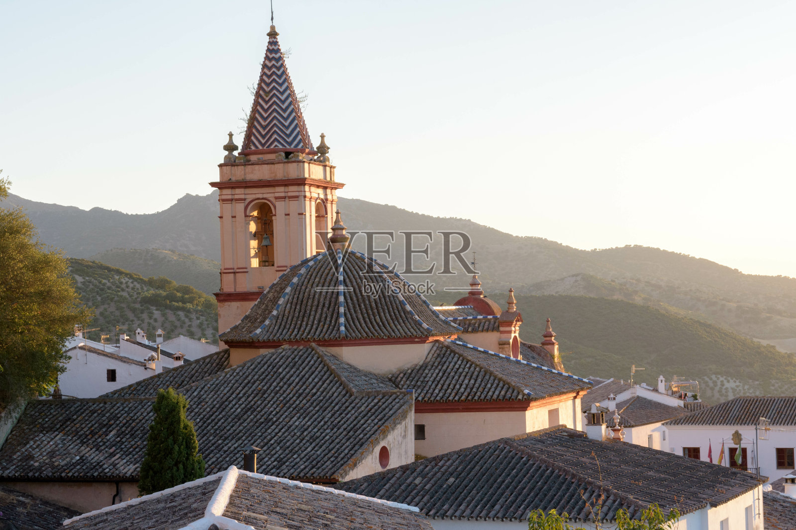 在西班牙，阳光下的Zahara de la Sierra教堂被建筑和山丘包围照片摄影图片