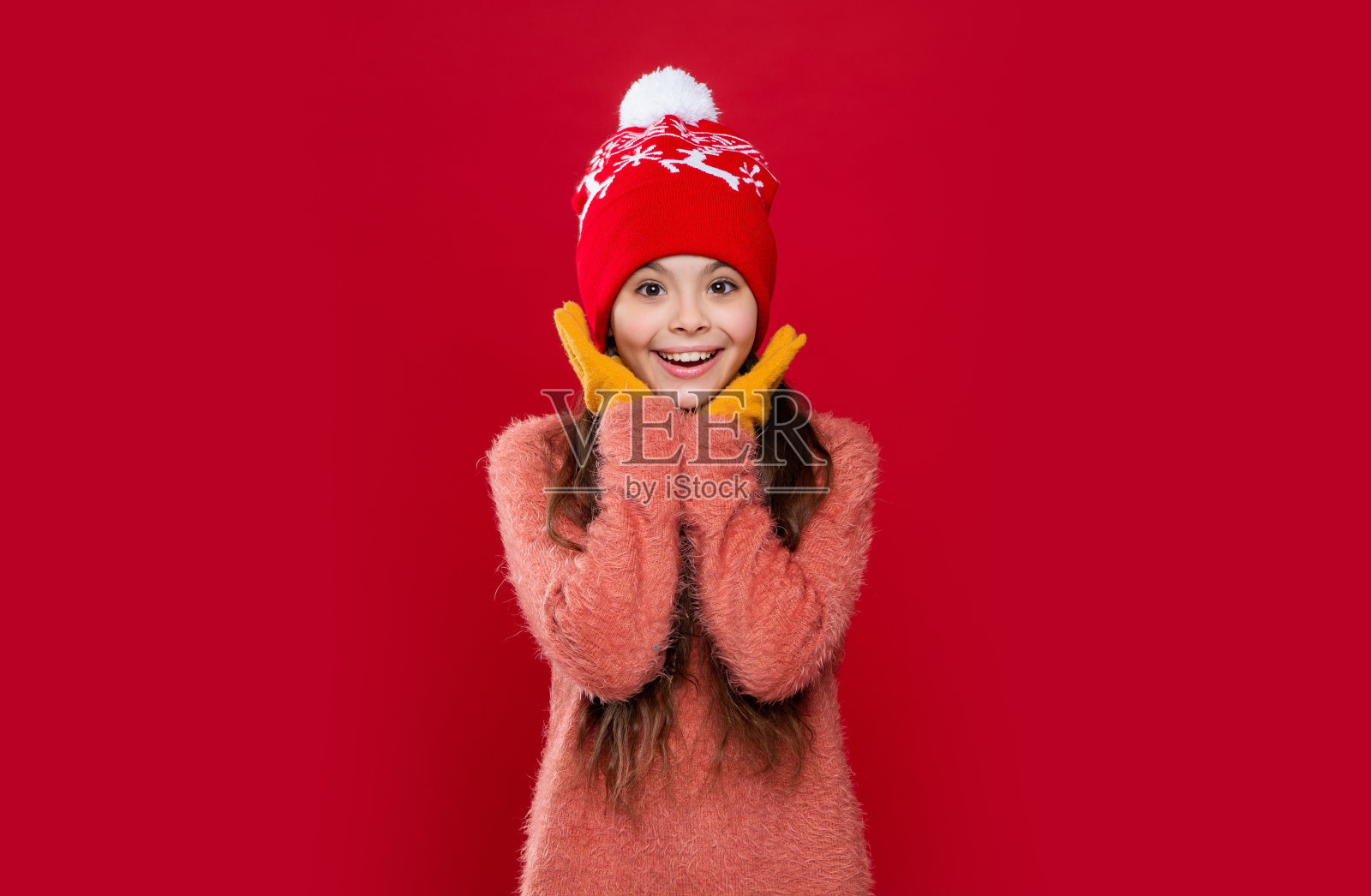 十几岁的孩子在帽子孤立的红色演播室背景。十几岁的孩子穿毛衣和帽子在工作室。照片摄影图片