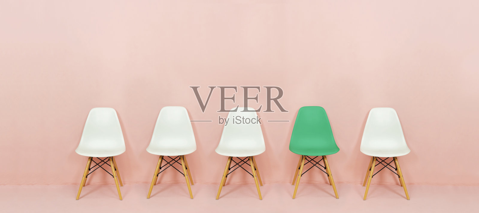 一排白色的椅子与粉红色背景上对比鲜明的绿色椅子。粉红色的墙上有五把空椅子照片摄影图片