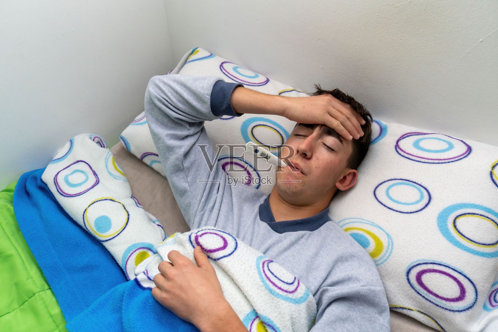 生病的白人躺在家里的床上，嘴里含着温度计，手放在额头上照片摄影图片