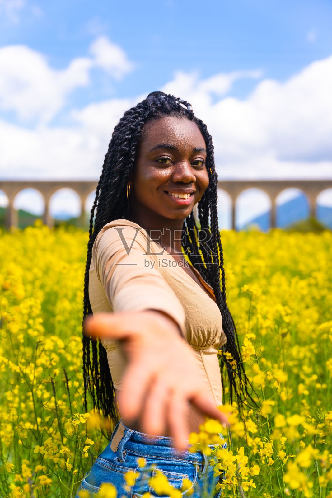 年轻美丽的非洲裔美国女性，在亮黄色的油菜籽地里扎着辫子照片摄影图片