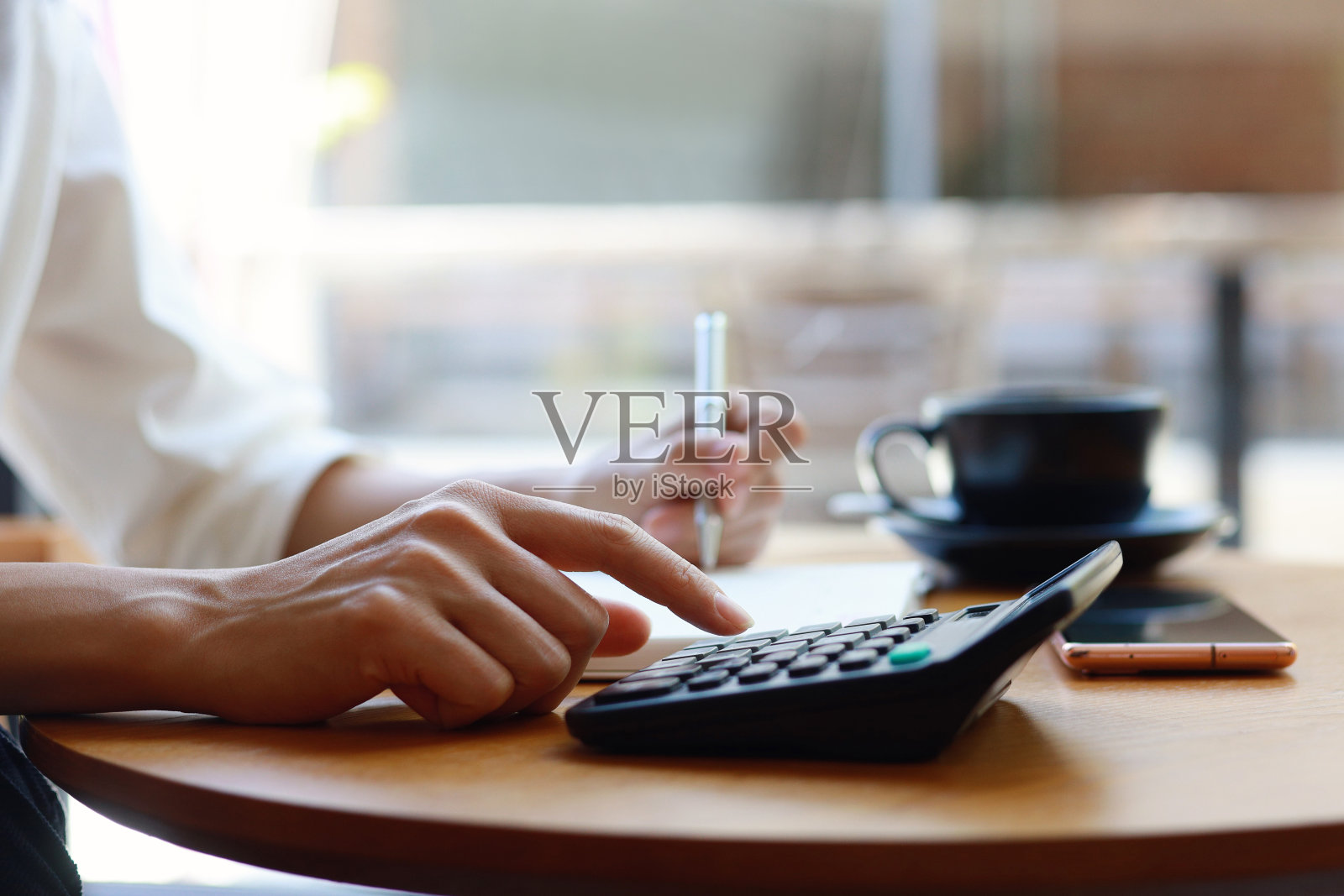 亚洲妇女坐在桌子旁用计算器做财务计划和预算，并在书上写字照片摄影图片