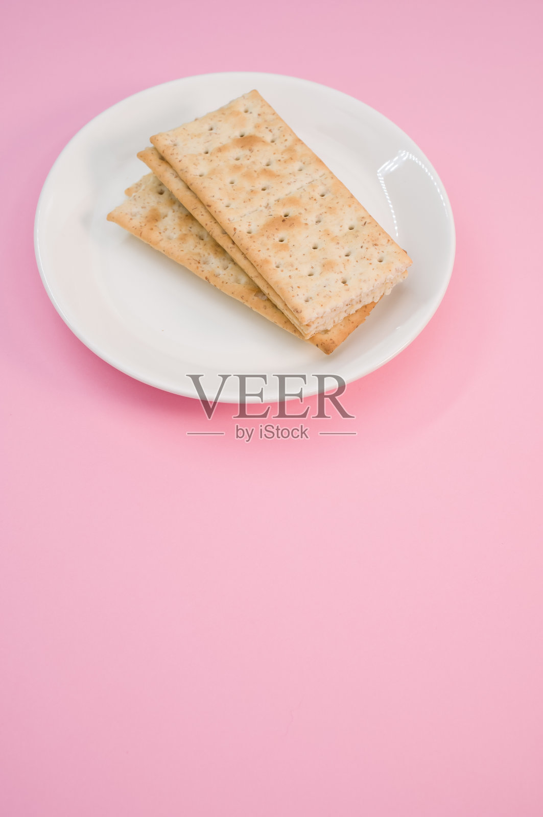 垂直拍摄的粉红表面上有咸饼干的盘子照片摄影图片