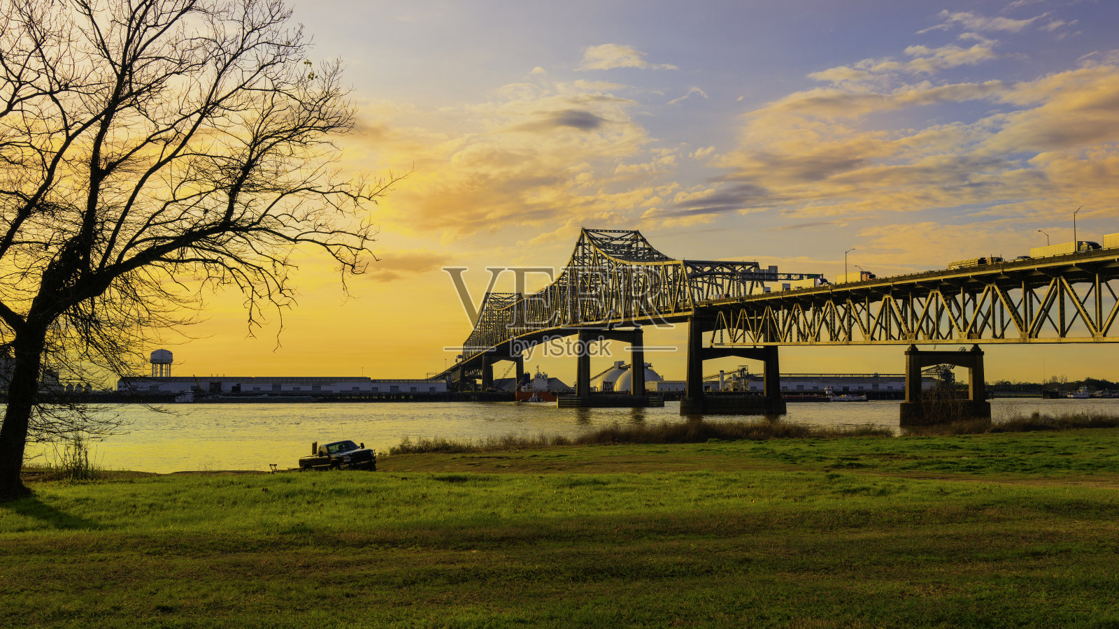 美国路易斯安那州巴吞鲁日，密西西比河上的霍勒斯威尔金森桥，日出时，一棵贫瘠的柳树在蓝天上，金色的云在发光照片摄影图片