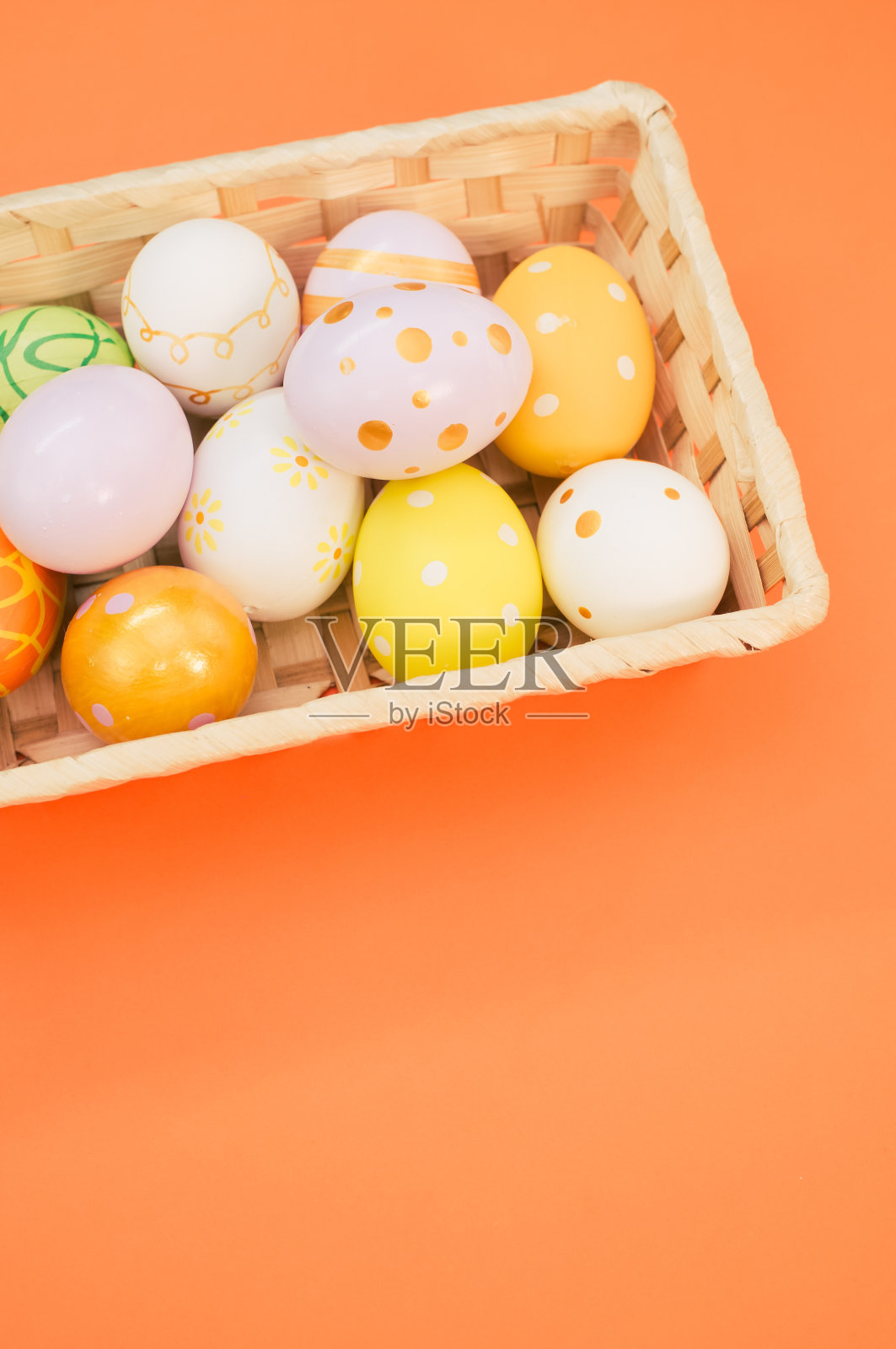 编织的篮子装满了五颜六色的复活节彩蛋在橙色的背景照片摄影图片