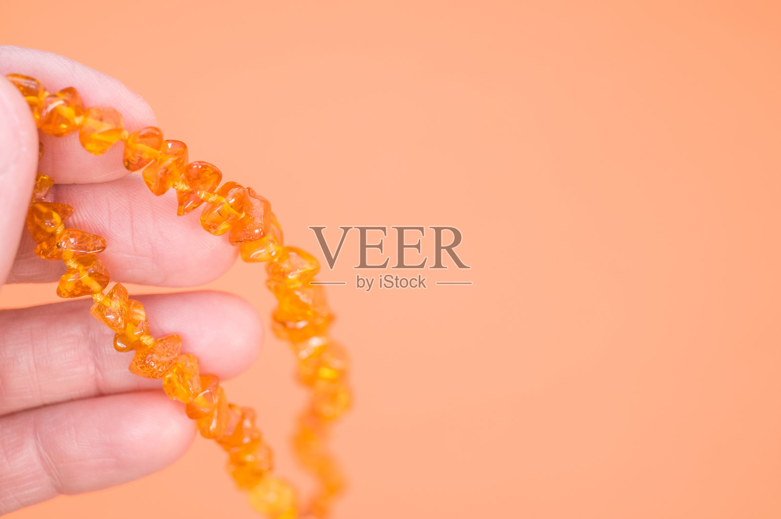 人拿着琥珀珠子项链对橙色背景照片摄影图片