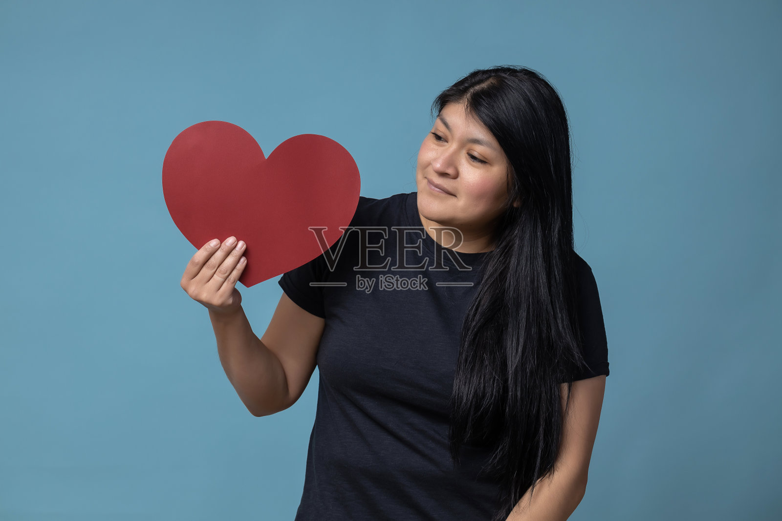 年轻的拉丁女子手持一张红色心形纸——情人节概念照片摄影图片