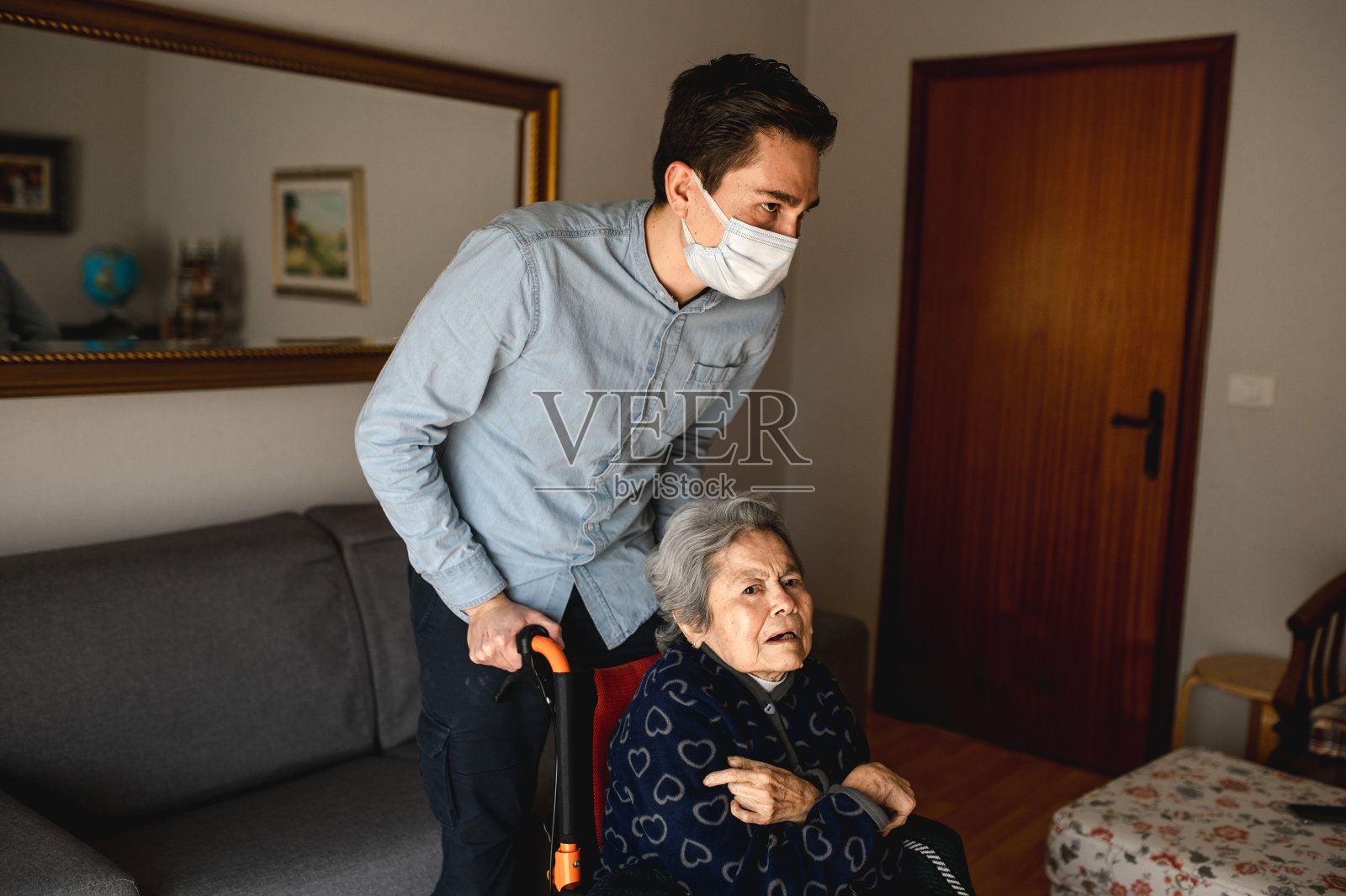 戴着口罩的男子照顾坐在轮椅上的祖母——家庭，居家关怀的理念照片摄影图片