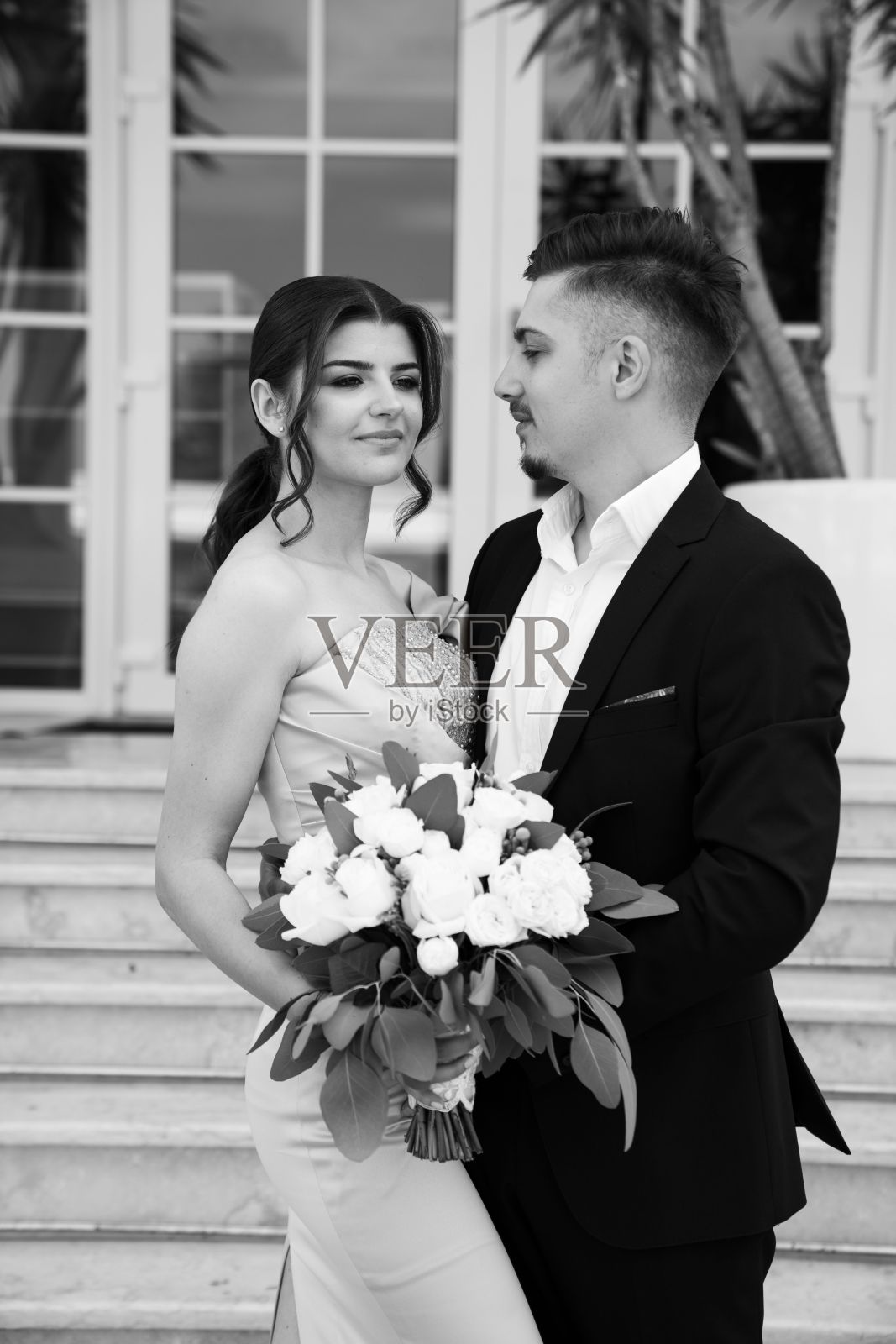 一对浪漫的白人夫妇手持花束的垂直灰度镜头。照片摄影图片