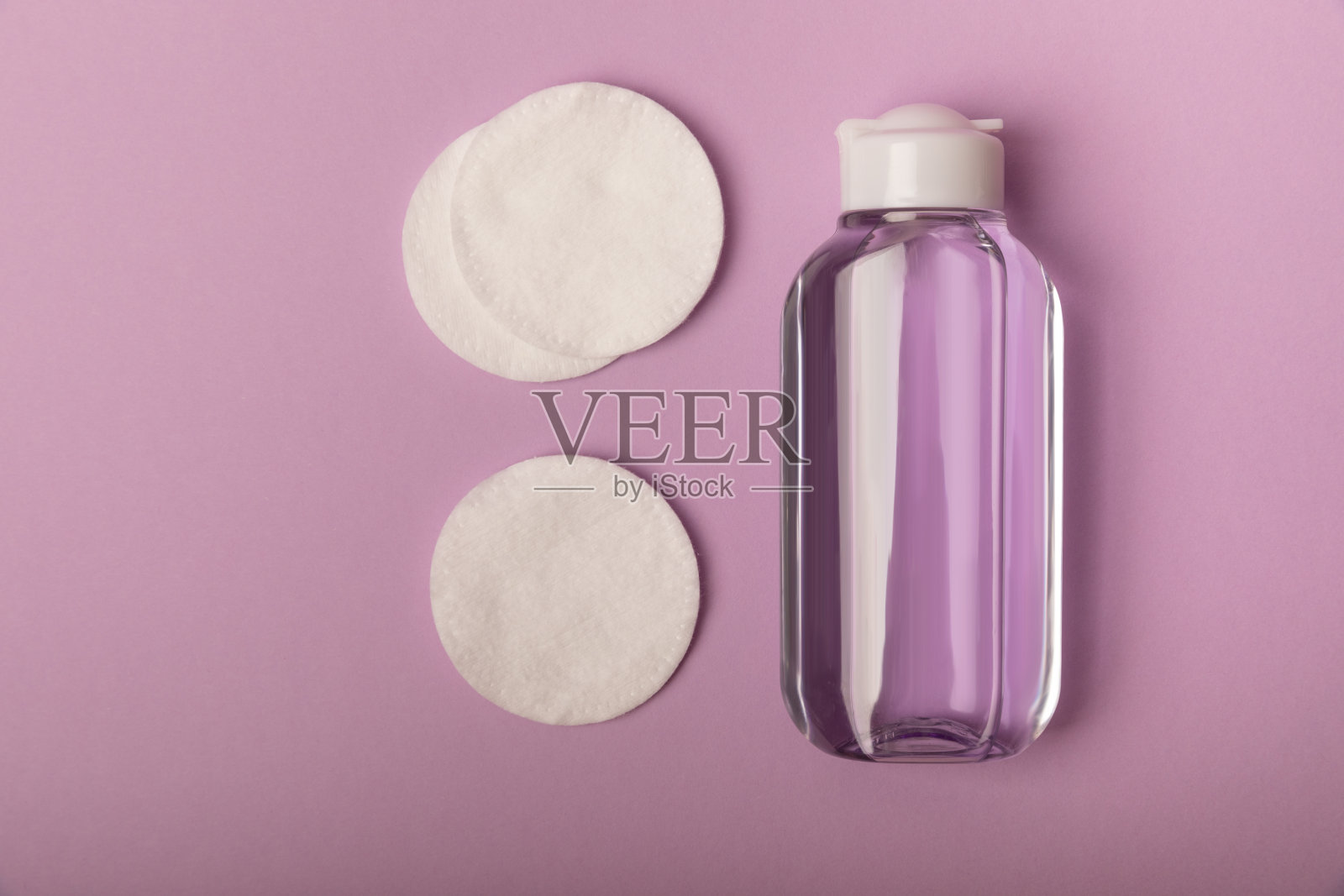 胶束水和棉垫在紫色的背景上。化妆和去皮脂爽肤水。滋补品、精华液或乳液。皮肤护理。美概念。俯视图。发短信的地方。本空间照片摄影图片