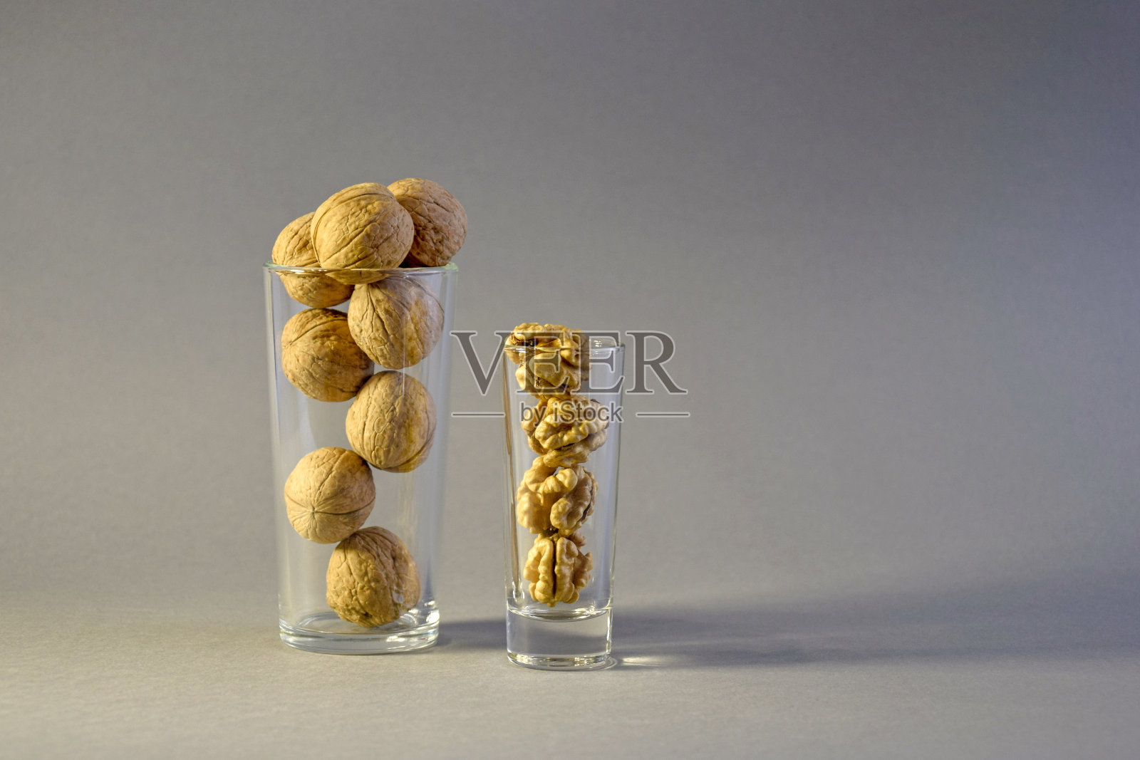 核桃和核桃仁被放在两个玻璃圆柱形玻璃杯中，背景是灰色的。照片摄影图片