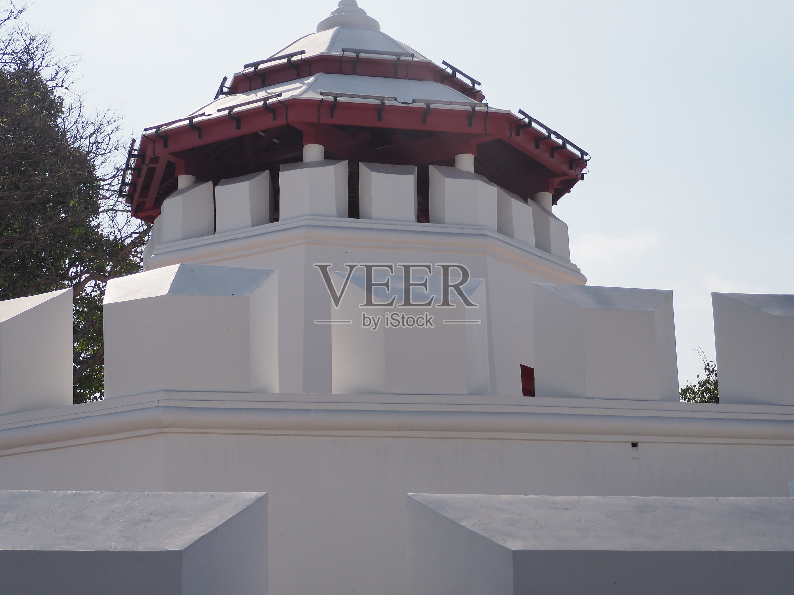 乳白色的塔楼上覆盖着绿色的叶子和银蓝色的天空，白灰色的云，黄白色的光。照片摄影图片