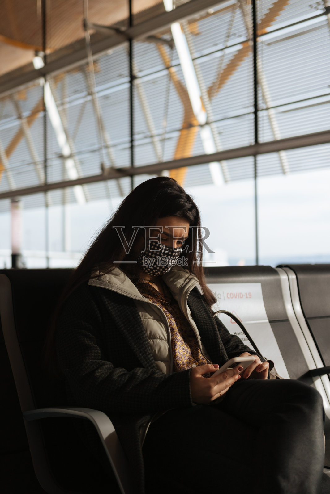 疫情期间旅行/戴口罩的女性在机场坐着看手机照片摄影图片