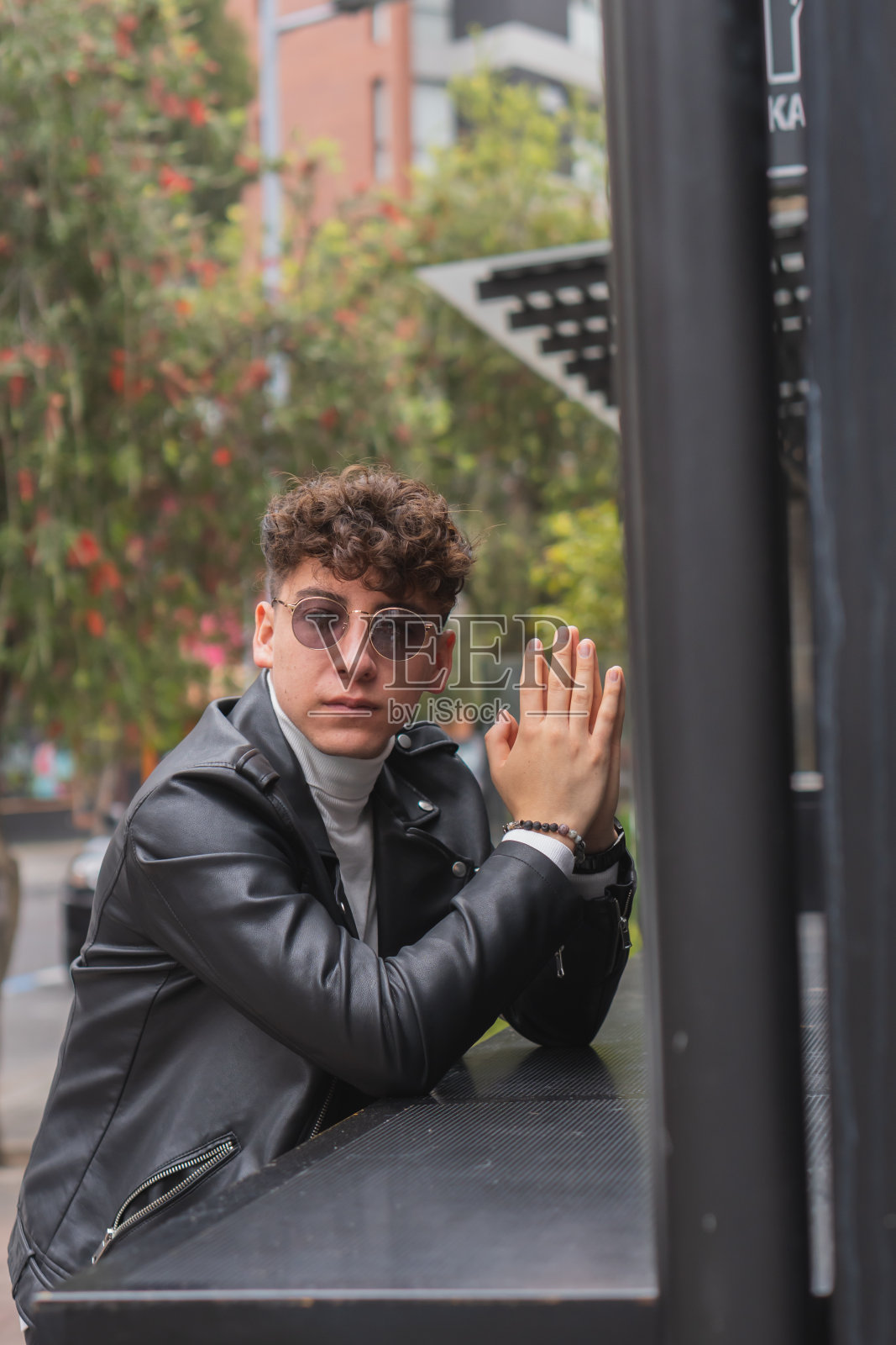 年轻的拉丁裔男子，一头卷发，戴着墨镜，穿着皮夹克坐在户外照片摄影图片