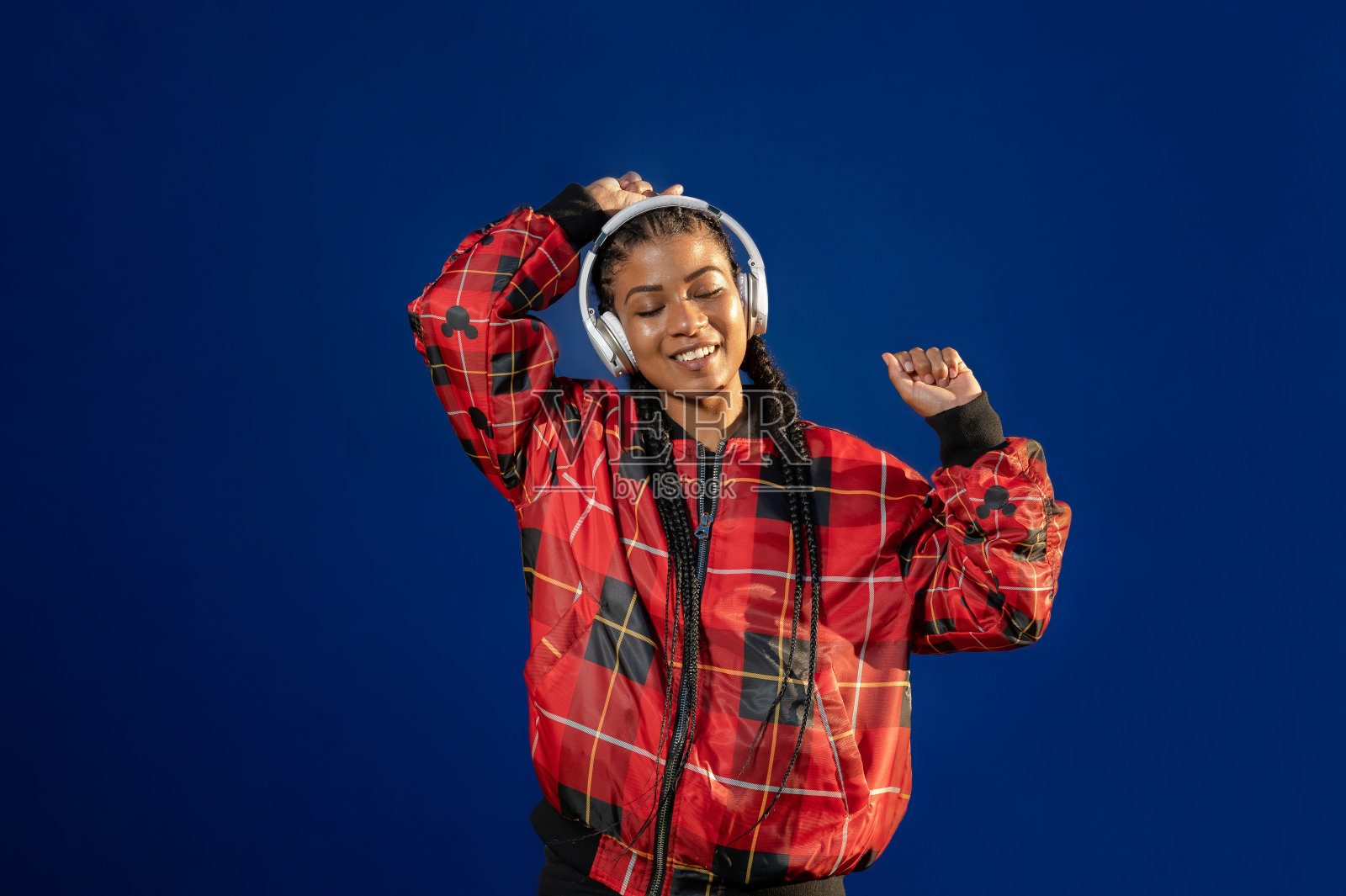 美丽的美国黑人女性听和享受音乐与耳机上的蓝色背景照片摄影图片