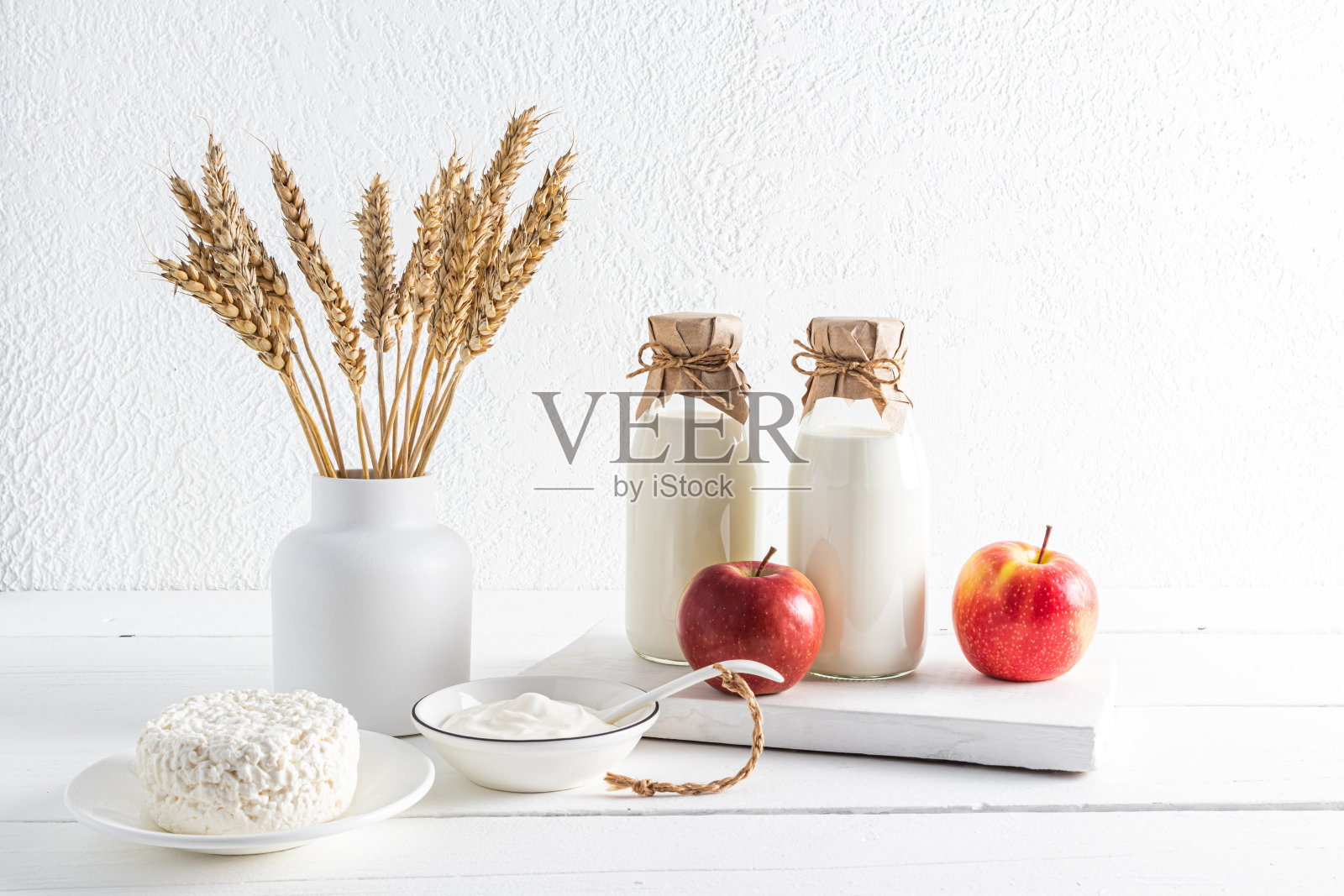 各种奶制品，苹果和一个白色背景上有一束耳朵的花瓶。前视图。犹太人七旬节的概念照片摄影图片