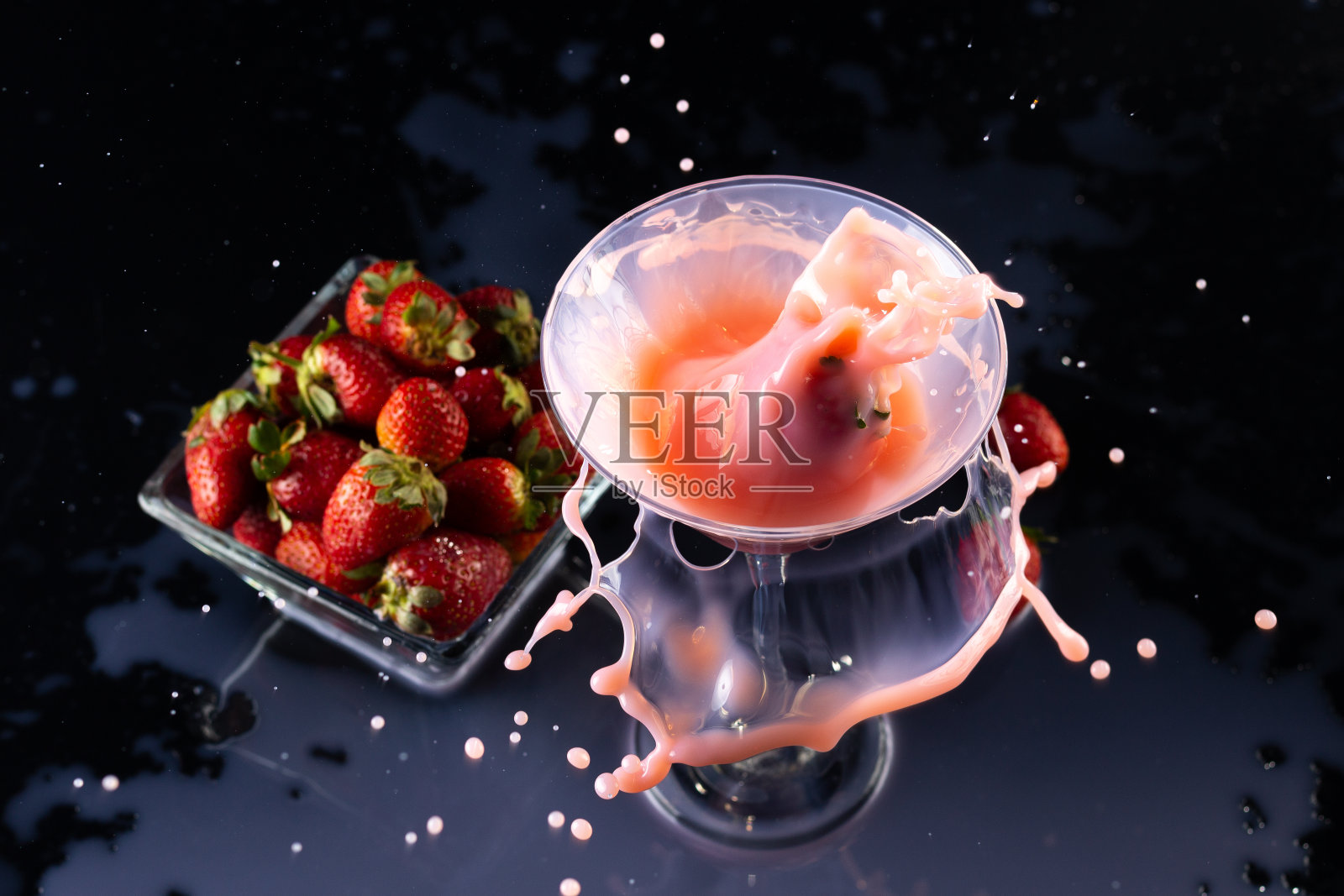 一个玻璃杯里的奶昔和一个小碗，黑色背景上有草莓照片摄影图片