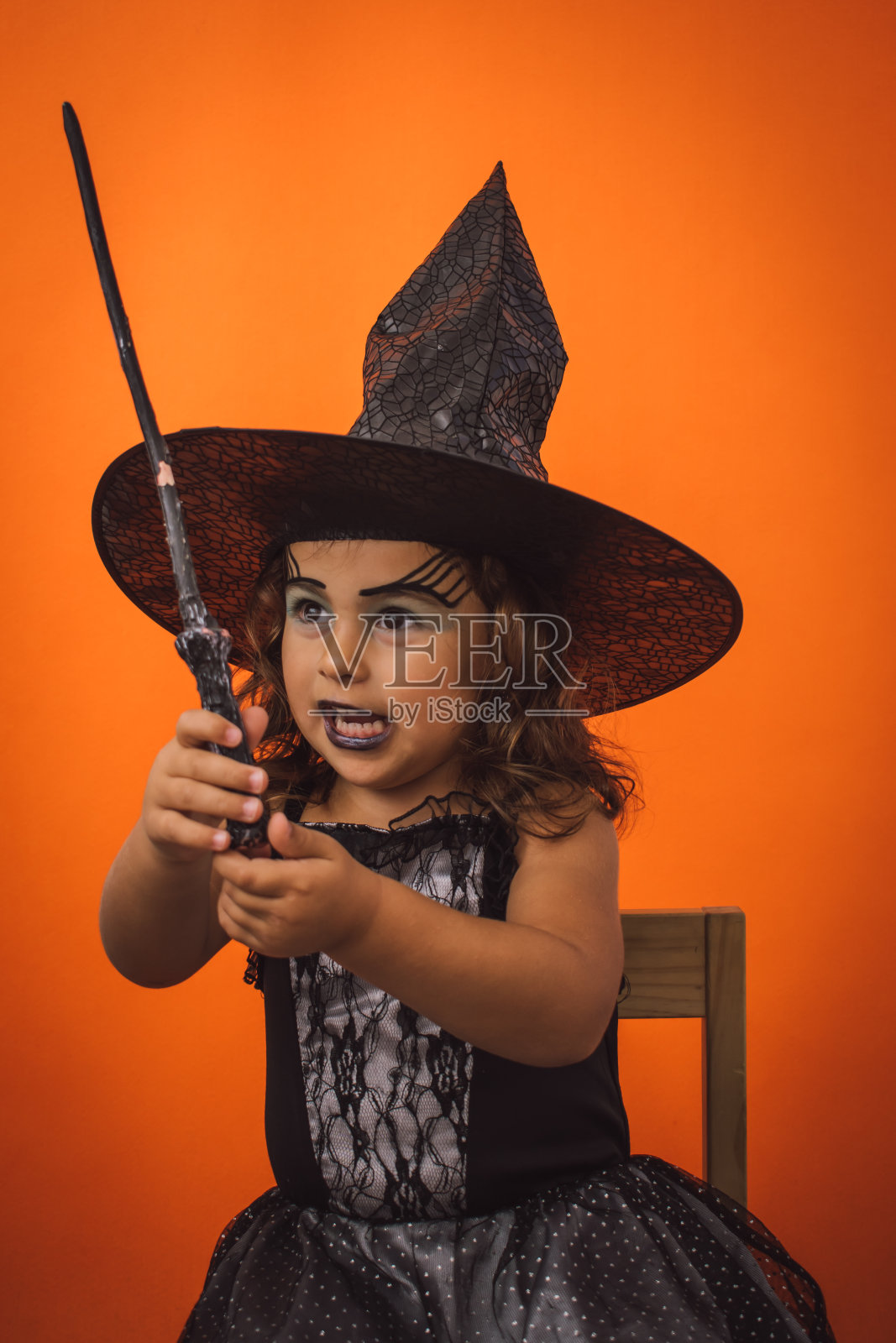 垂直拍摄一个穿着女巫服装的女孩子，橙色背景上有一根魔杖照片摄影图片