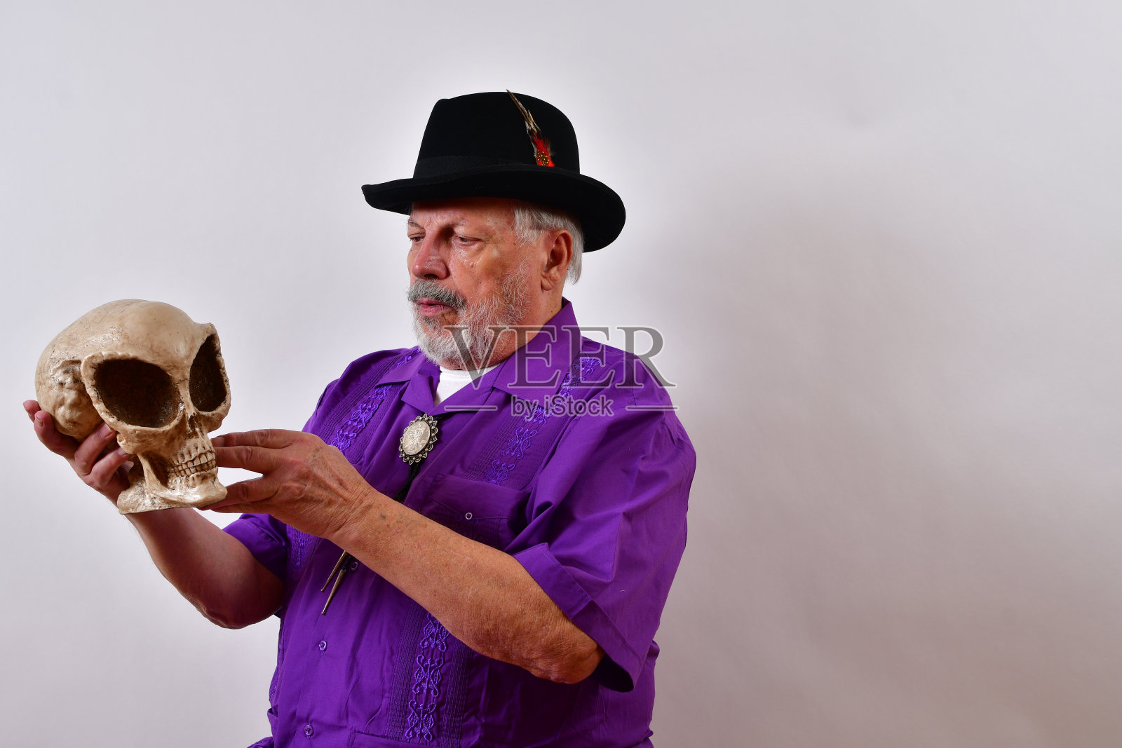 一个穿着紫色衬衫和帽子的老人拿着白色的外星人头骨照片摄影图片