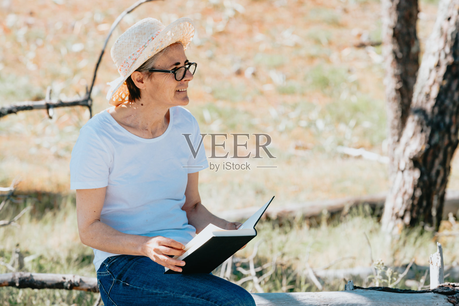 来自西班牙的美丽老妇人戴着草帽，在一个阳光明媚的日子里在户外看书照片摄影图片