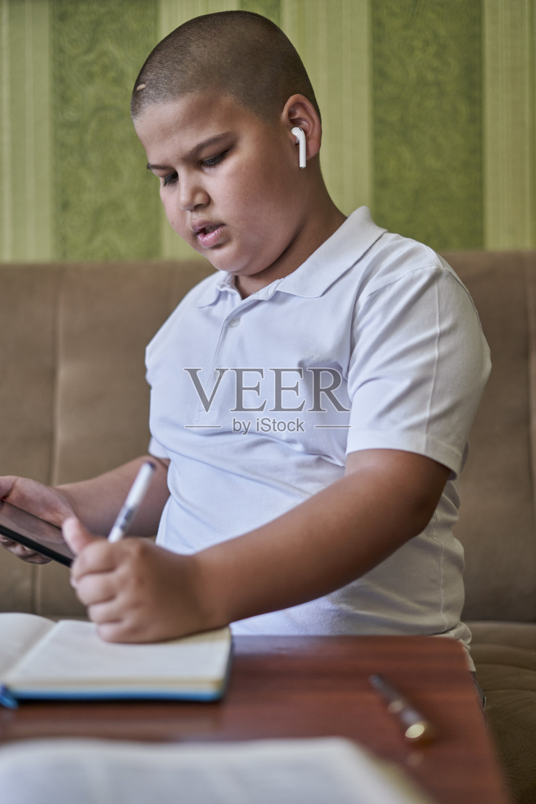 年轻的男学生一边在家听在线课程一边记笔记——远程课程的概念照片摄影图片