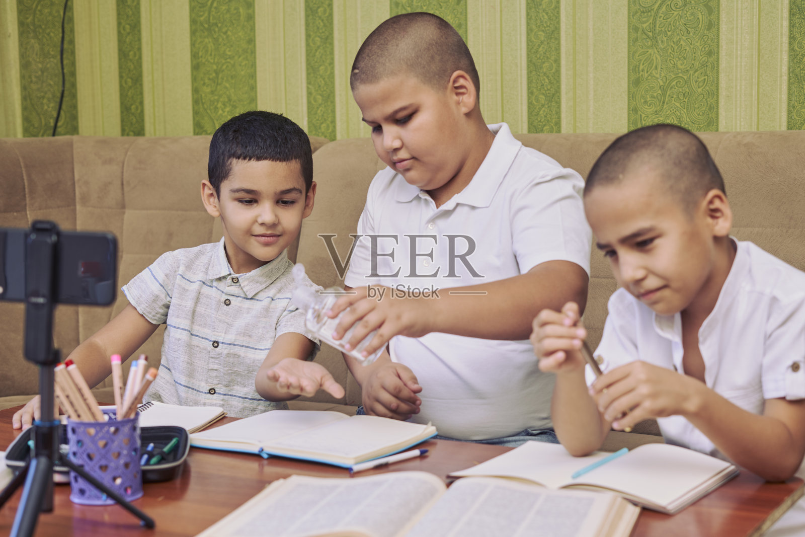 年轻的男学生一边使用洗手液，一边在家听在线课程照片摄影图片