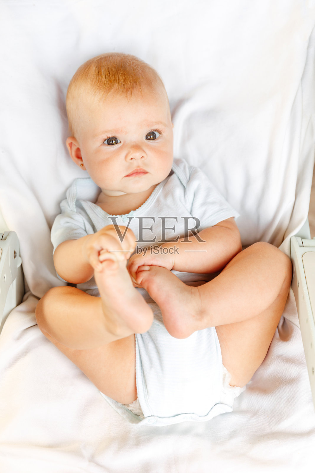 可爱的新生小女孩，滑稽的脸看着白色背景的相机。婴儿休息玩耍躺在家里的婴儿床上。母亲快乐孩子的概念。照片摄影图片