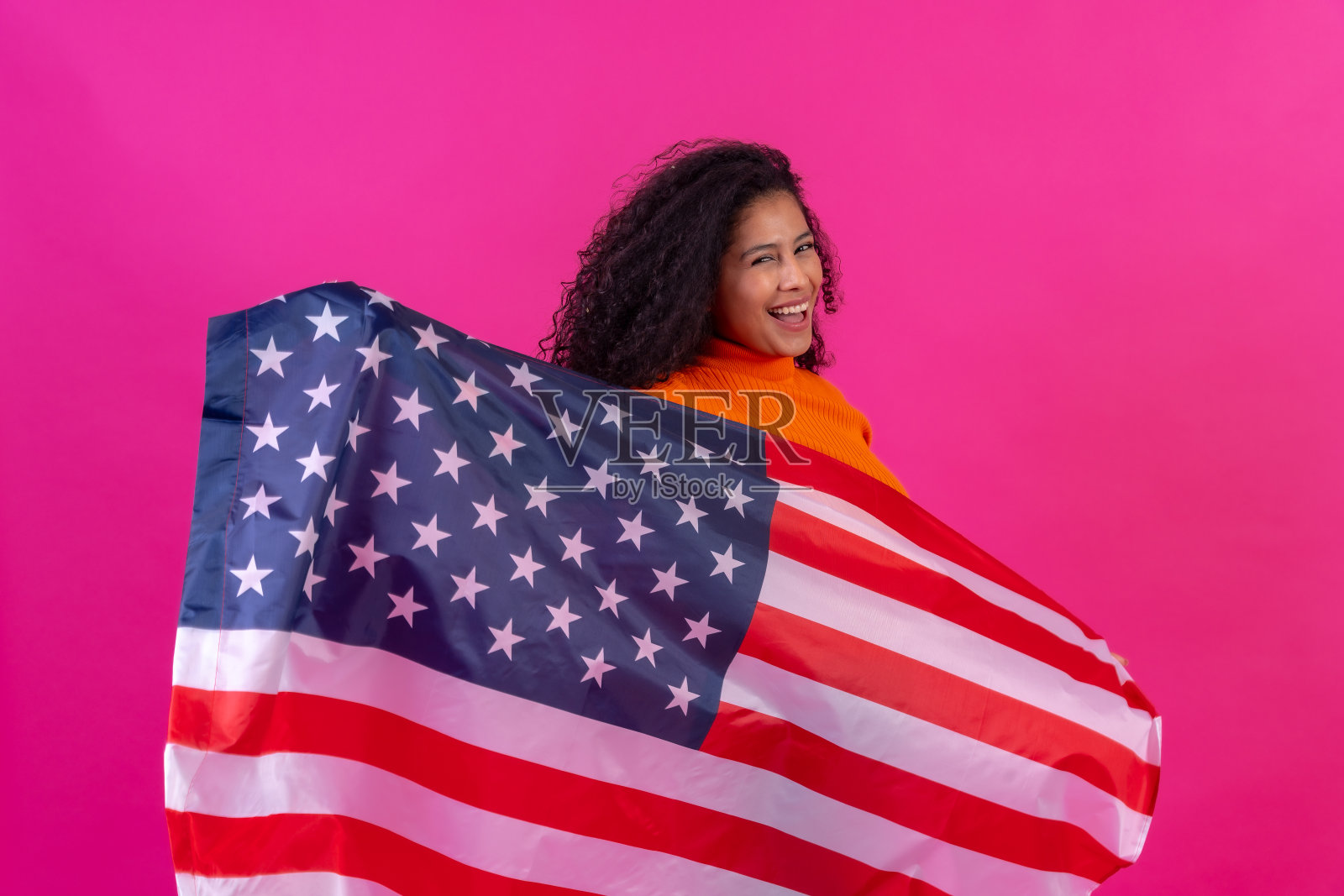 卷发女人与美国国旗在一个粉红色的背景，工作室拍摄照片摄影图片