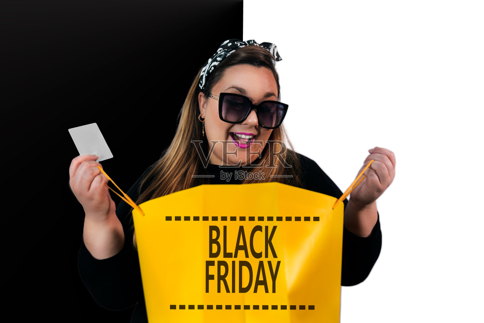 大码的女人惊讶地拿着一个黄色的购物袋，上面有黑色星期五的标志和信用卡照片摄影图片