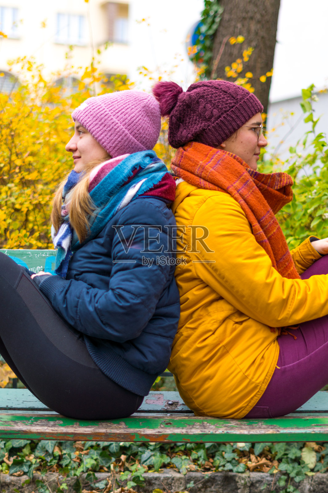 垂直拍摄两个穿着彩色冬装的白人女性背靠背坐着照片摄影图片