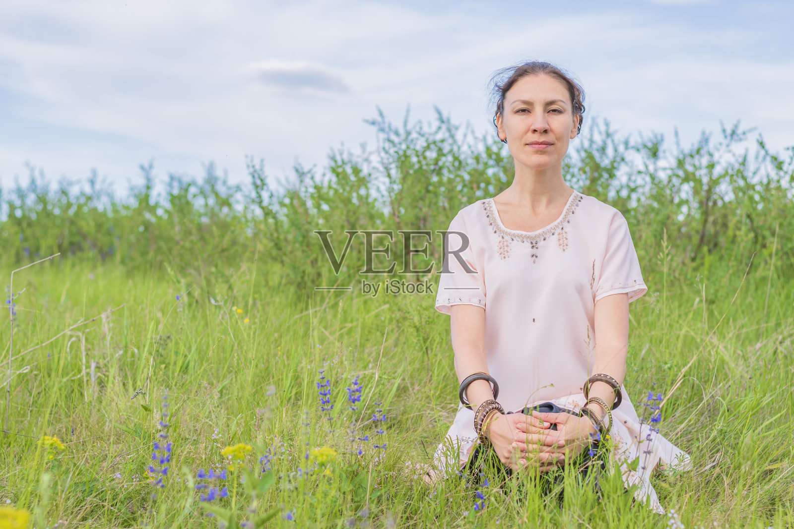 年轻女子坐在绿色草坪上的莲花位置冥想。户外瑜伽课。照片摄影图片
