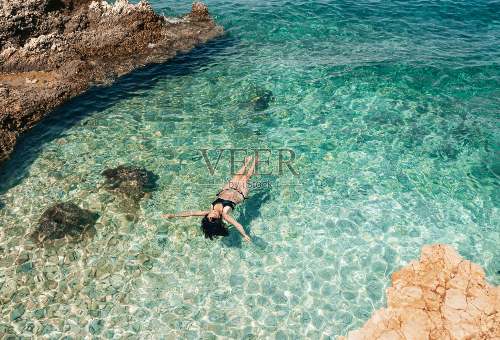 高角度的观点，年轻女子在黑色比基尼漂浮在蓝绿色透明的海水。照片摄影图片