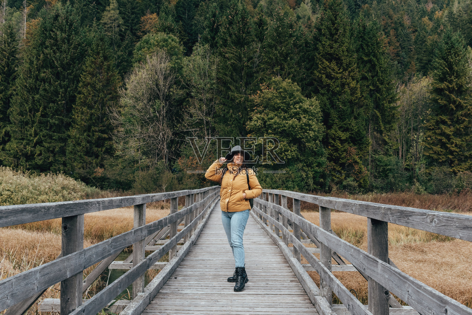 身着秋装的女子，站在小溪上的木制人行桥上照片摄影图片