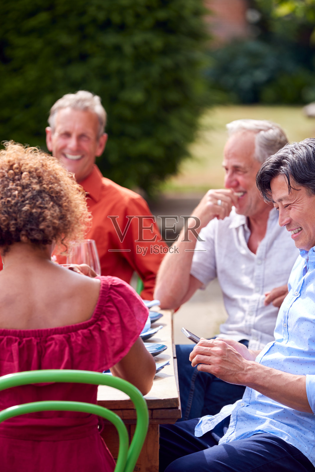 一群成熟的朋友在家里花园的夏季晚宴上交谈照片摄影图片
