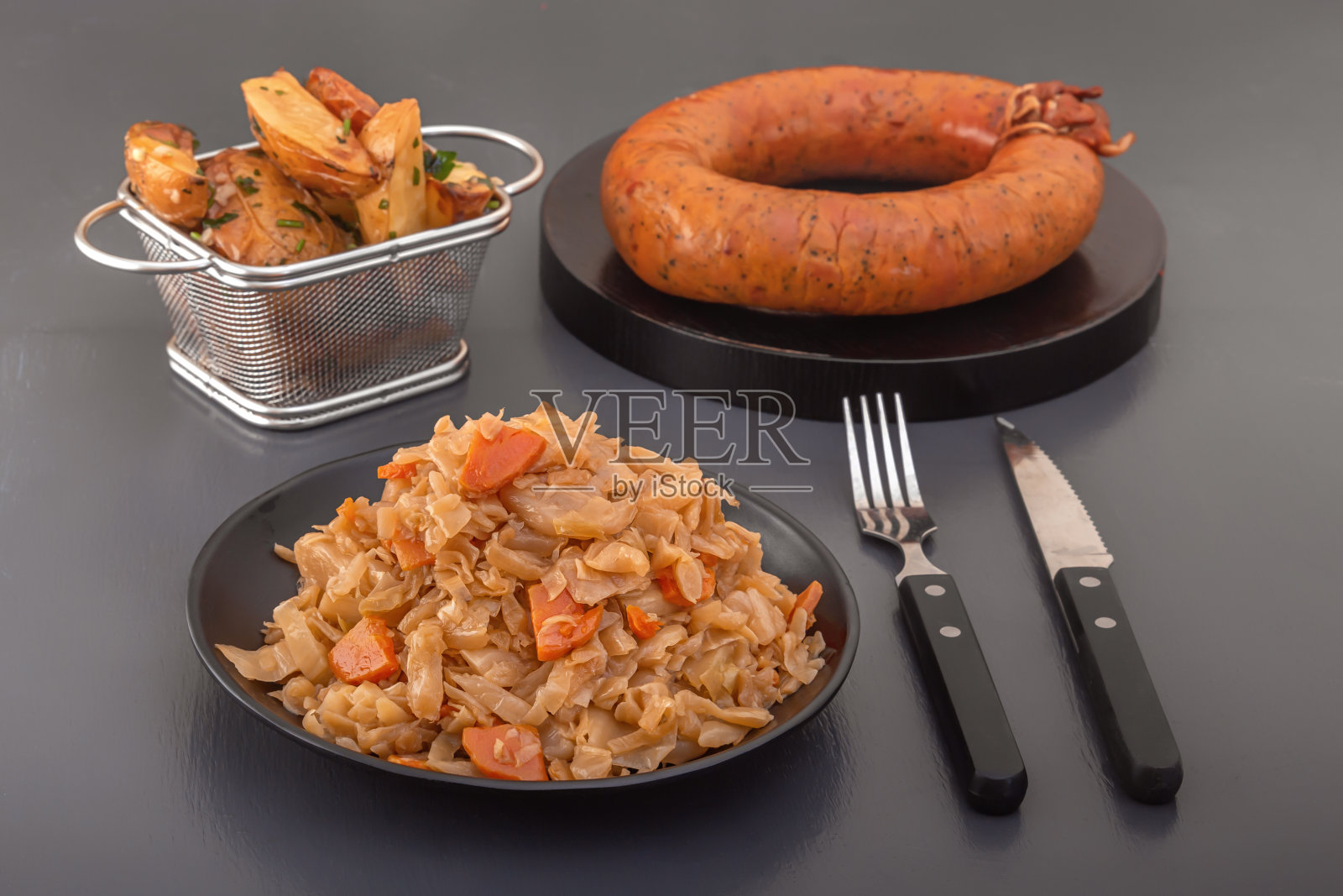 炖卷心菜——黑盘子里的烤白菜，背景是一圈熏香肠和烤土豆。乡村风味早餐照片摄影图片