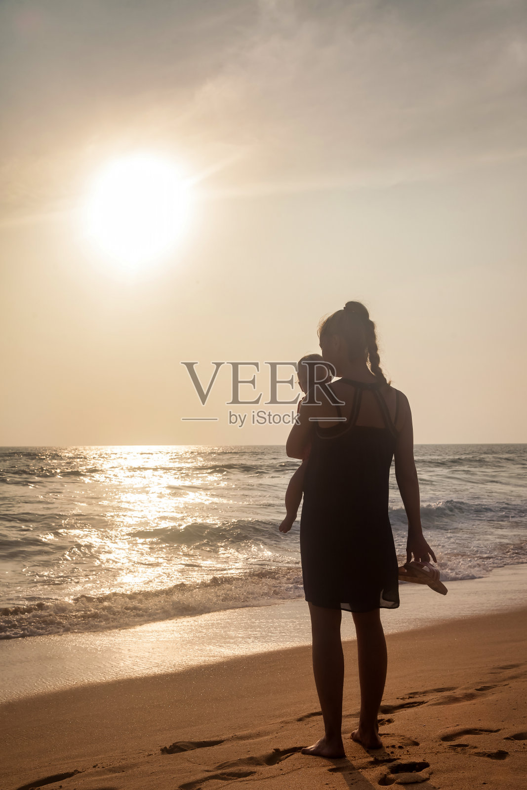 剪影妈妈与婴儿在怀里站在热带海滩在海上的背景。女人带着小孩在夏天享受假期。母亲的概念和与孩子的娱乐。复制文本空格照片摄影图片